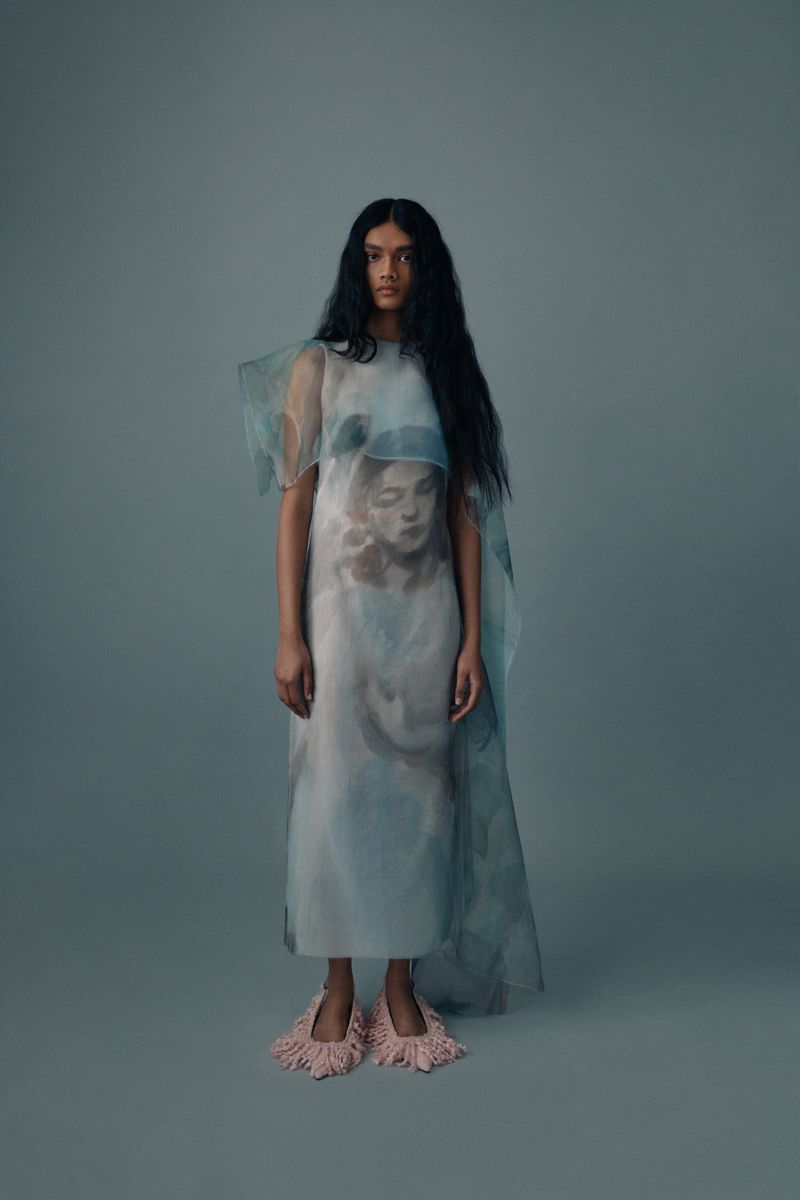 Fashion portrait of an adult female wearing a translucent dress with an image print, posing in front of a grey backdrop.
