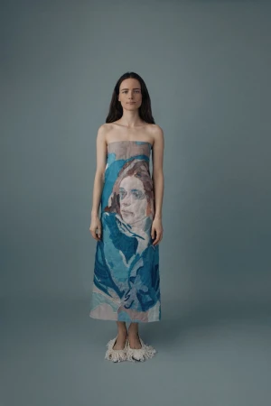 Full-length portrait of a woman with long brown hair wearing a strapless dress with a blue and beige print of a portrait.