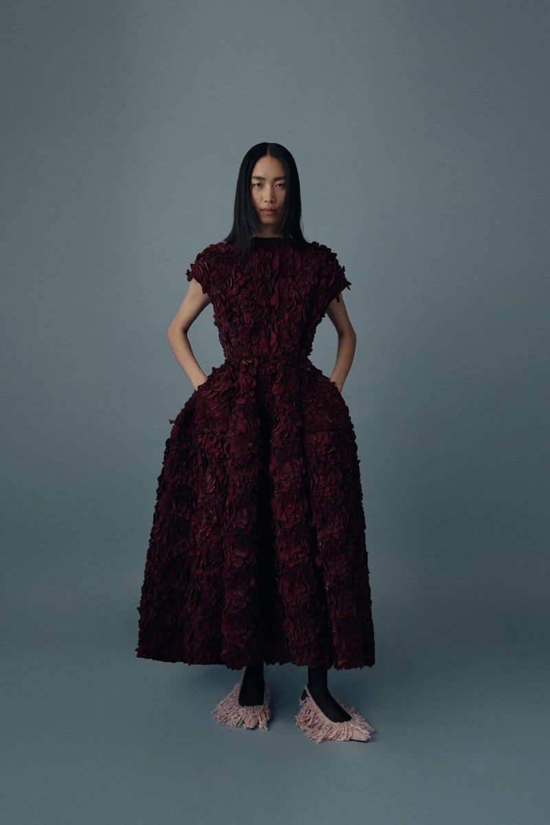 Woman in a textural burgundy dress poses in a studio setting, showcasing fashion with a clean background and soft lighting.