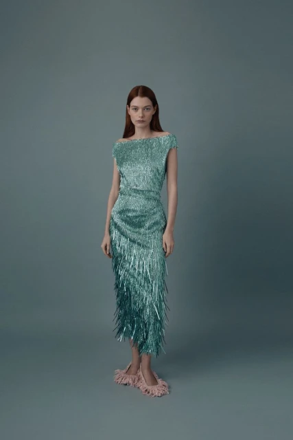 Elegant woman in a shimmering turquoise fringed dress and feathered slippers poses in a studio with a soft, neutral backdrop.