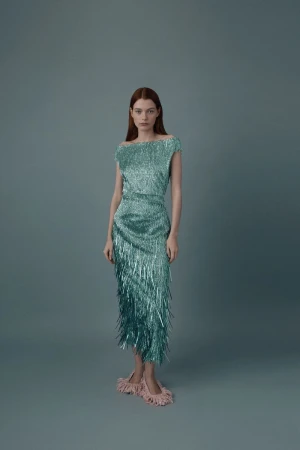Elegant woman in a shimmering turquoise fringed dress and feathered slippers poses in a studio with a soft, neutral backdrop.