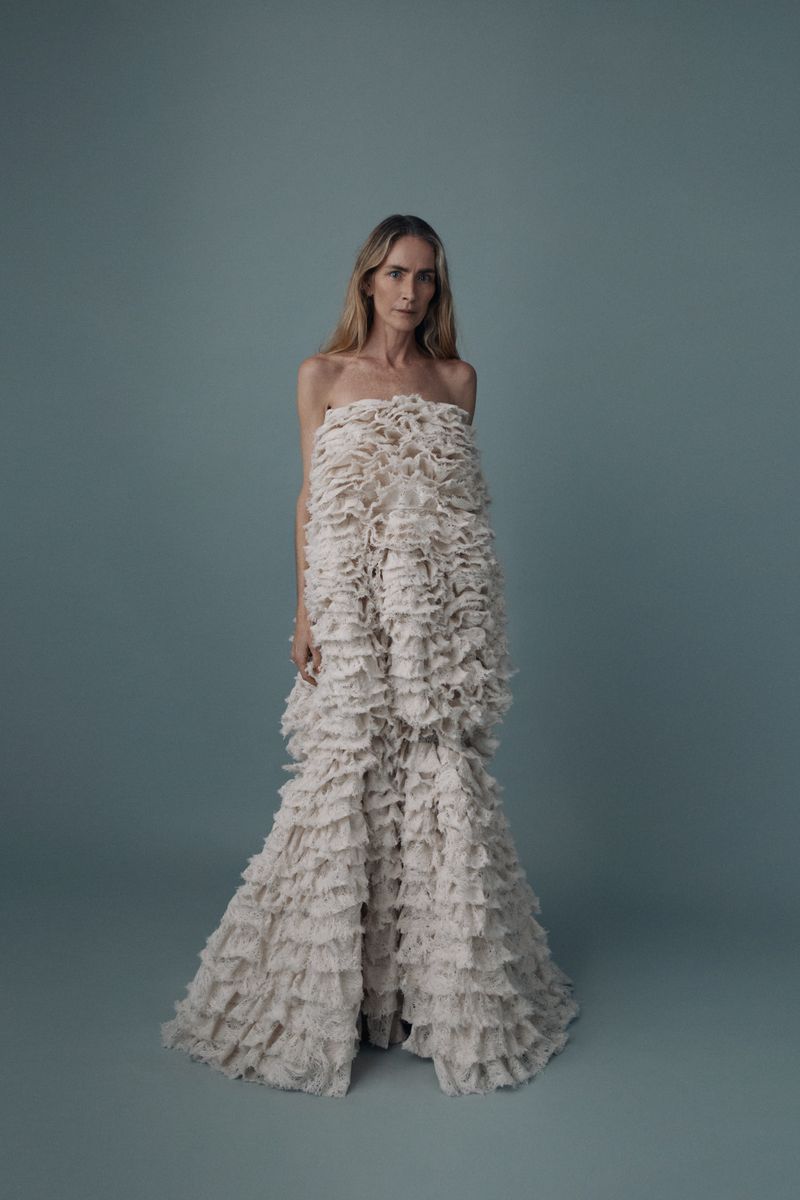 Elegant woman in a white strapless dress with ruffles, posing in a full shot against a light blue backdrop in a studio setting.