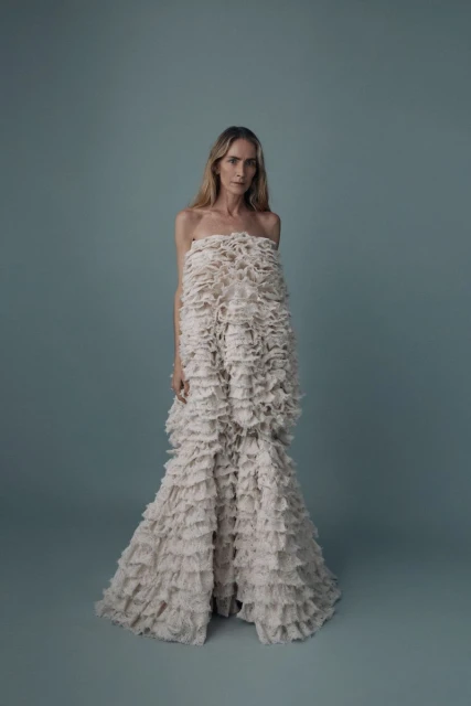 Elegant woman in a white strapless dress with ruffles, posing in a full shot against a light blue backdrop in a studio setting.