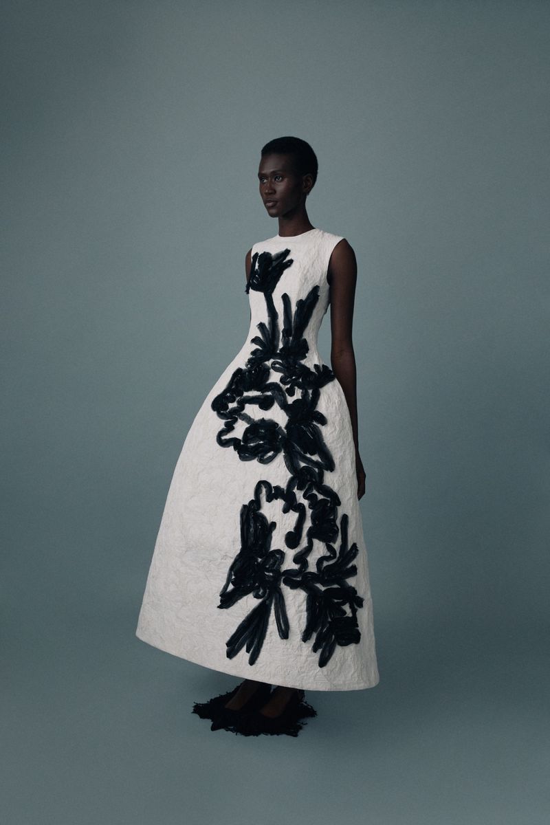 Elegant Black woman in a white sleeveless couture gown with black floral applique posing in a studio with neutral background, fashion editorial.