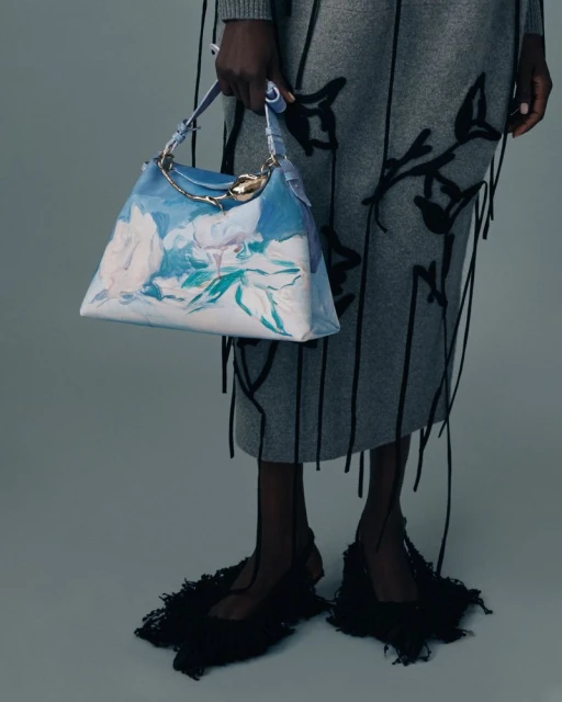 Fashion shot featuring a woman displaying a blue and white floral handbag, paired with a grey skirt and black fringed shoes.
