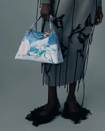 Fashion shot featuring a woman displaying a blue and white floral handbag, paired with a grey skirt and black fringed shoes.