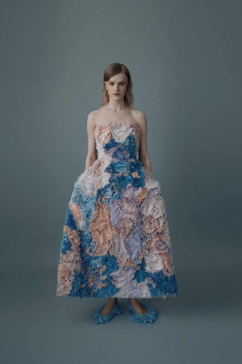Adult female model poses in a full-length strapless gown with a light blue, dark blue, and peach floral pattern in a photo studio.