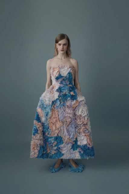Adult female model poses in a full-length strapless gown with a light blue, dark blue, and peach floral pattern in a photo studio.