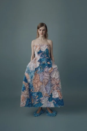 Adult female model poses in a full-length strapless gown with a light blue, dark blue, and peach floral pattern in a photo studio.