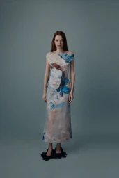 Model wearing an artistic portrait-print column dress with black fringed shoes against a slate backdrop for Erdem AW25.