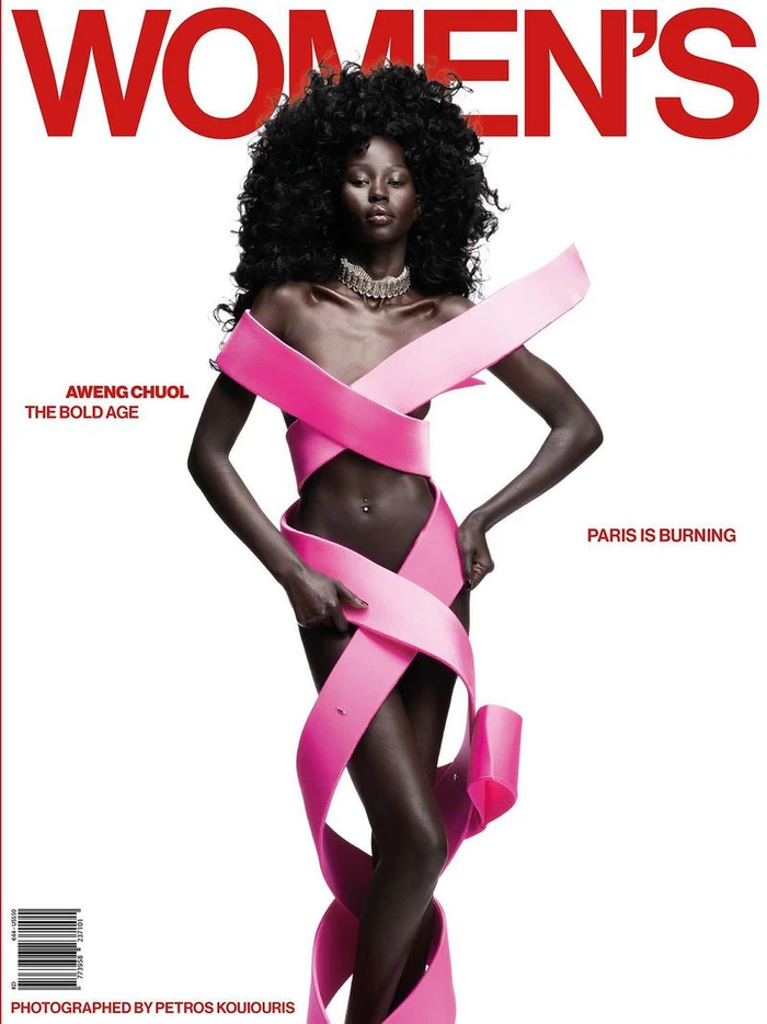 Model Aweng Chuol wrapped in a sculptural pink ribbon dress with voluminous afro hair on a white studio magazine cover.