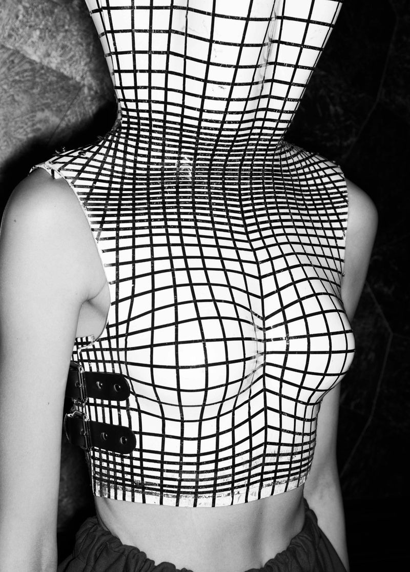 Monochrome portrait of a person wearing a grid-patterned top and hood, a conceptual fashion image, and stark monochromatic color palette.