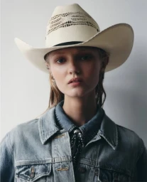 Close-up portrait of a woman wearing a straw cowboy hat and a denim jacket for Summer Winter Magazine