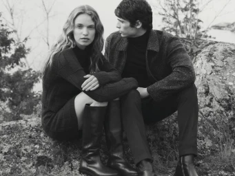 Black and white portrait of a woman and a man seated outdoors on a rocky outcrop wearing knitwear and tall boots for Tiger of Sweden