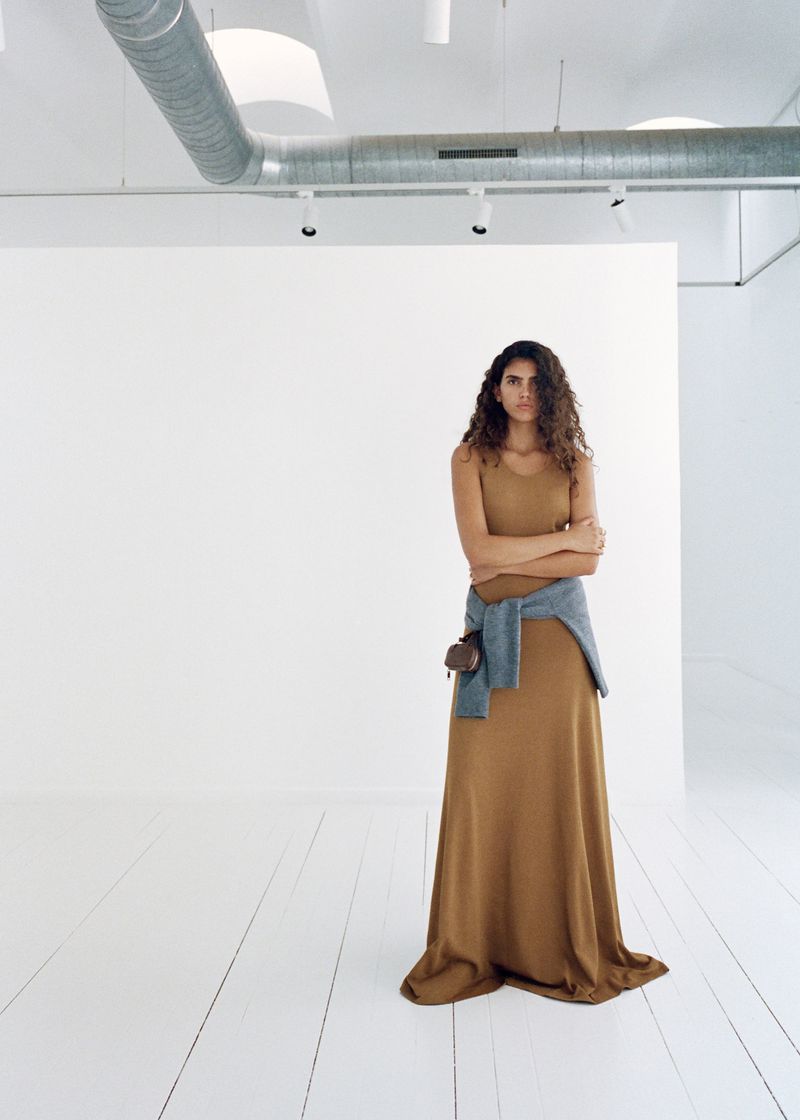 Adult woman in a dress posing in a bright white photo studio with neutral colors, simple fashion, and natural curly hair.