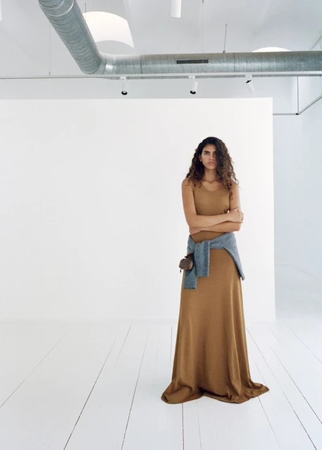 Adult woman in a dress posing in a bright white photo studio with neutral colors, simple fashion, and natural curly hair.