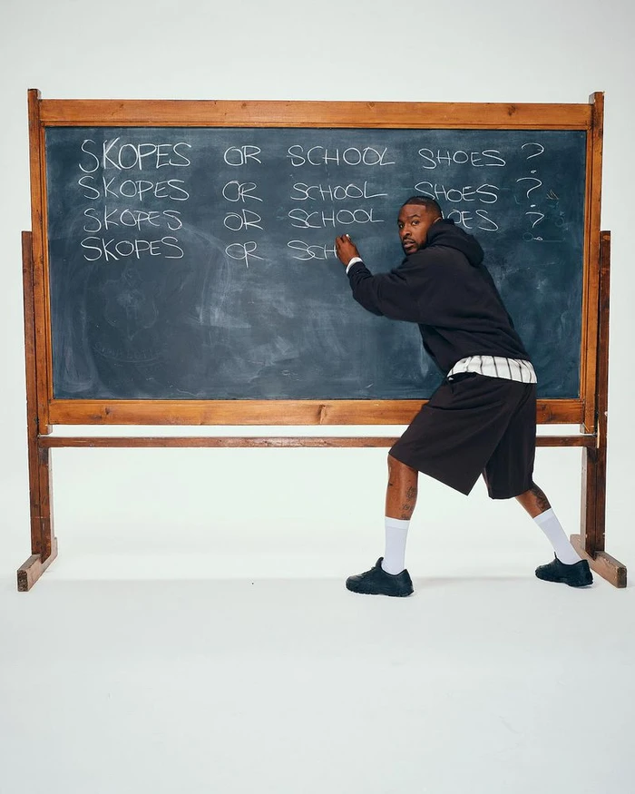 Skepta writing on a large blackboard in front of a white wall for the Puma x Skepta Skope campaign