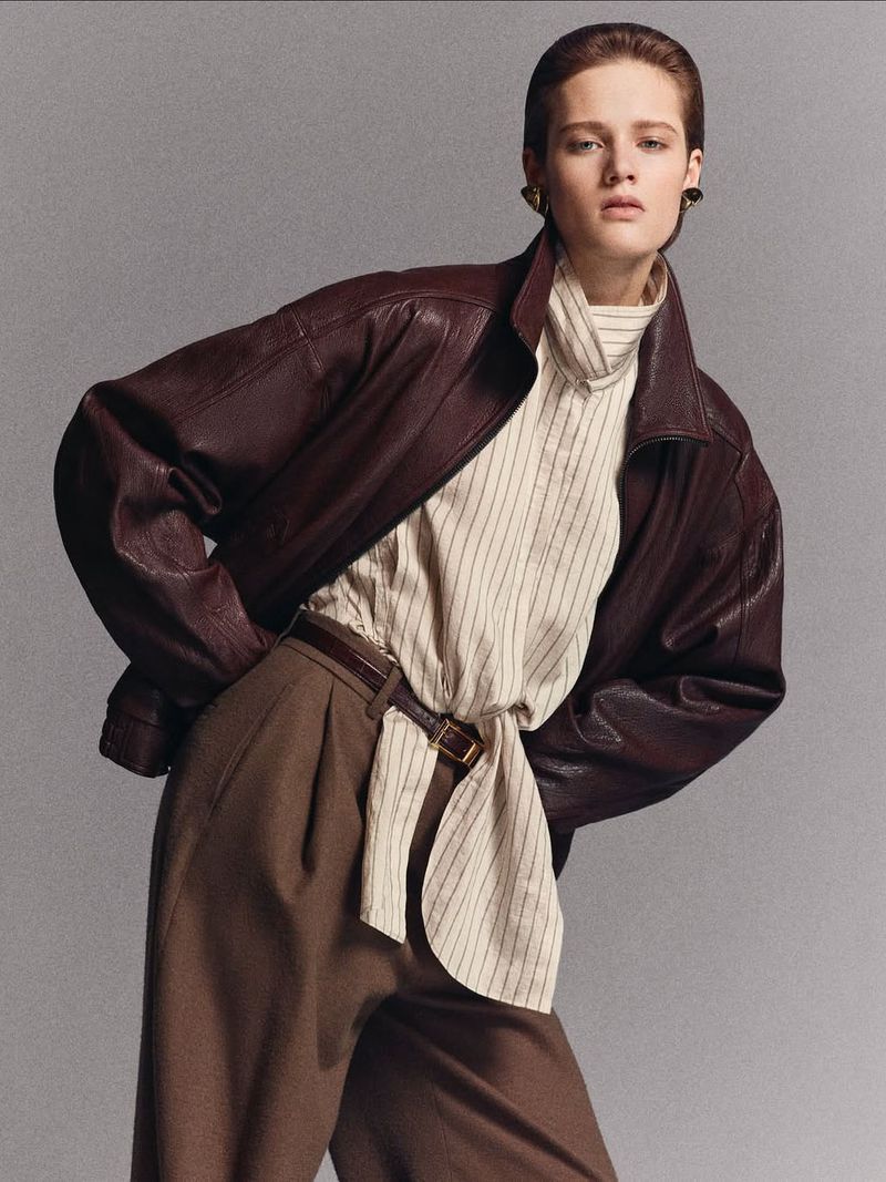Fashionable woman in a burgundy leather jacket and brown trousers poses in a studio. Elegant, stylish attire for confident women.