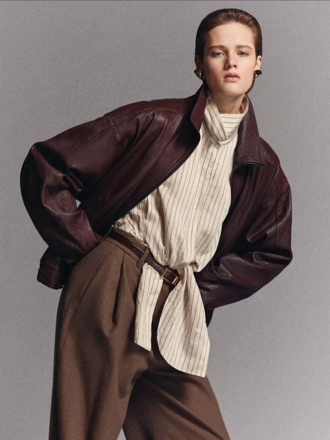 Fashionable woman in a burgundy leather jacket and brown trousers poses in a studio. Elegant, stylish attire for confident women.