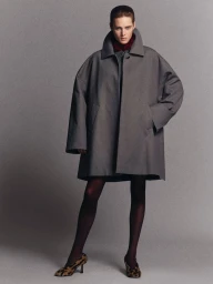 Model wearing an oversized grey coat and patterned heels against a plain grey studio backdrop for Recto F/W 2025 Campaign