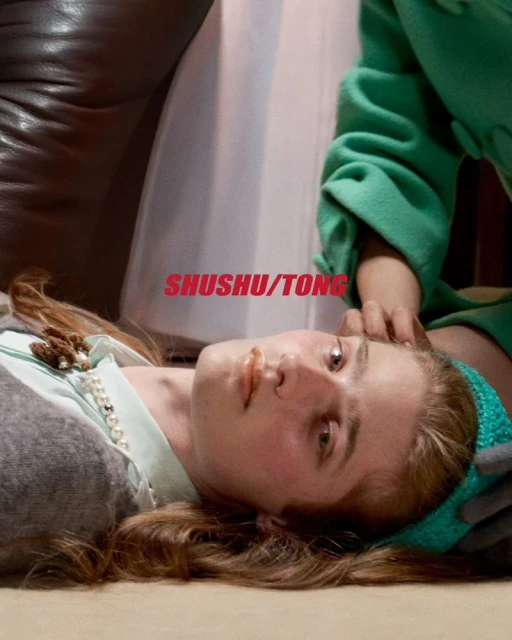 Close-up of a fair-skinned adult female lying down indoors with light brown hair, wearing a light-blue top and headband, and grey sweater.
