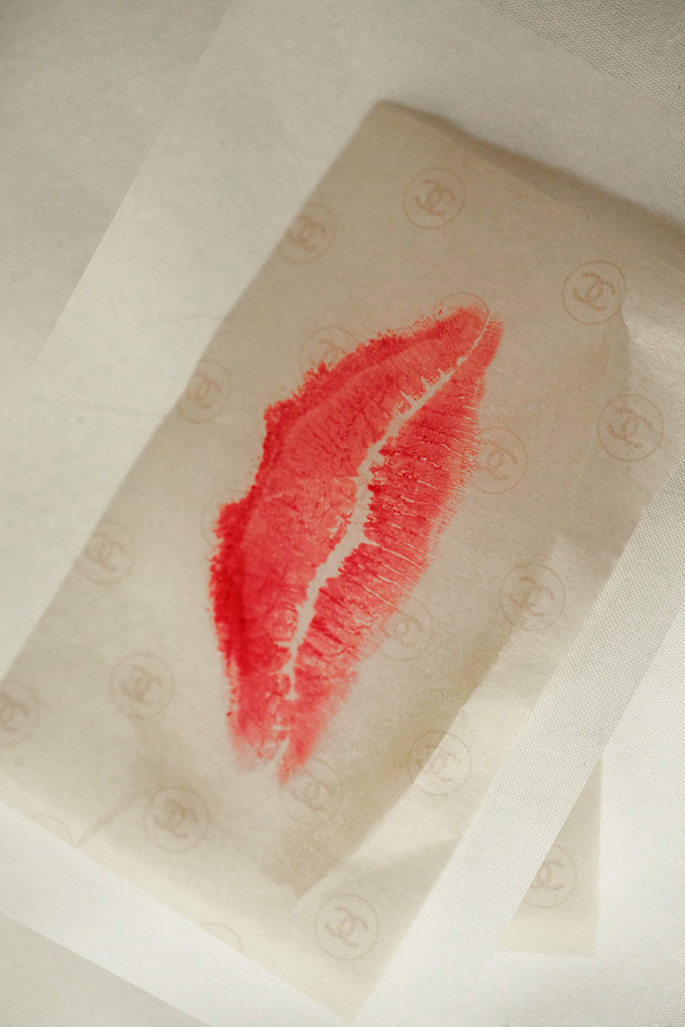 A red lipstick kiss imprint on paper, with a repeating logo pattern, creates an intimate and bold visual statement.