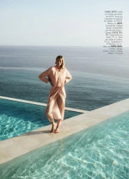 Model standing barefoot on a pool edge by the ocean wearing a pink silk outfit for Elle Germany fashion editorial