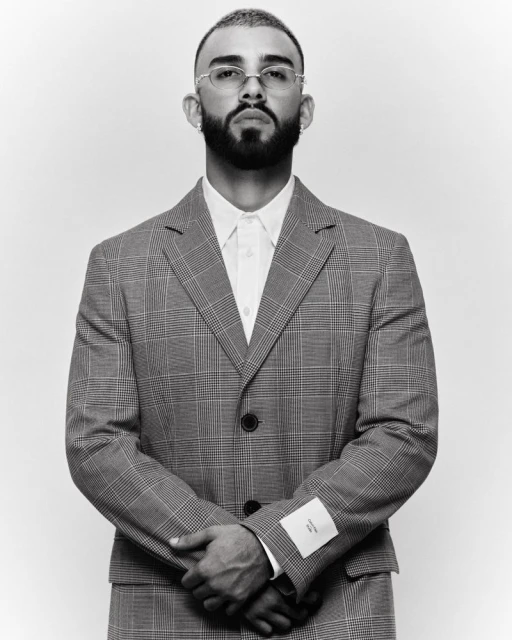 Monochrome portrait of a bearded man in a grey plaid suit with folded arms against a white background in a photo studio setting.