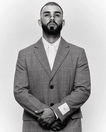Monochrome portrait of a bearded man in a grey plaid suit with folded arms against a white background in a photo studio setting.