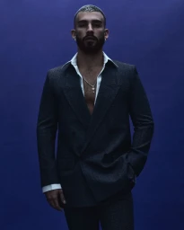 Man wearing a dark double-breasted suit and white collared shirt against a dark blue background for Numero Netherlands.