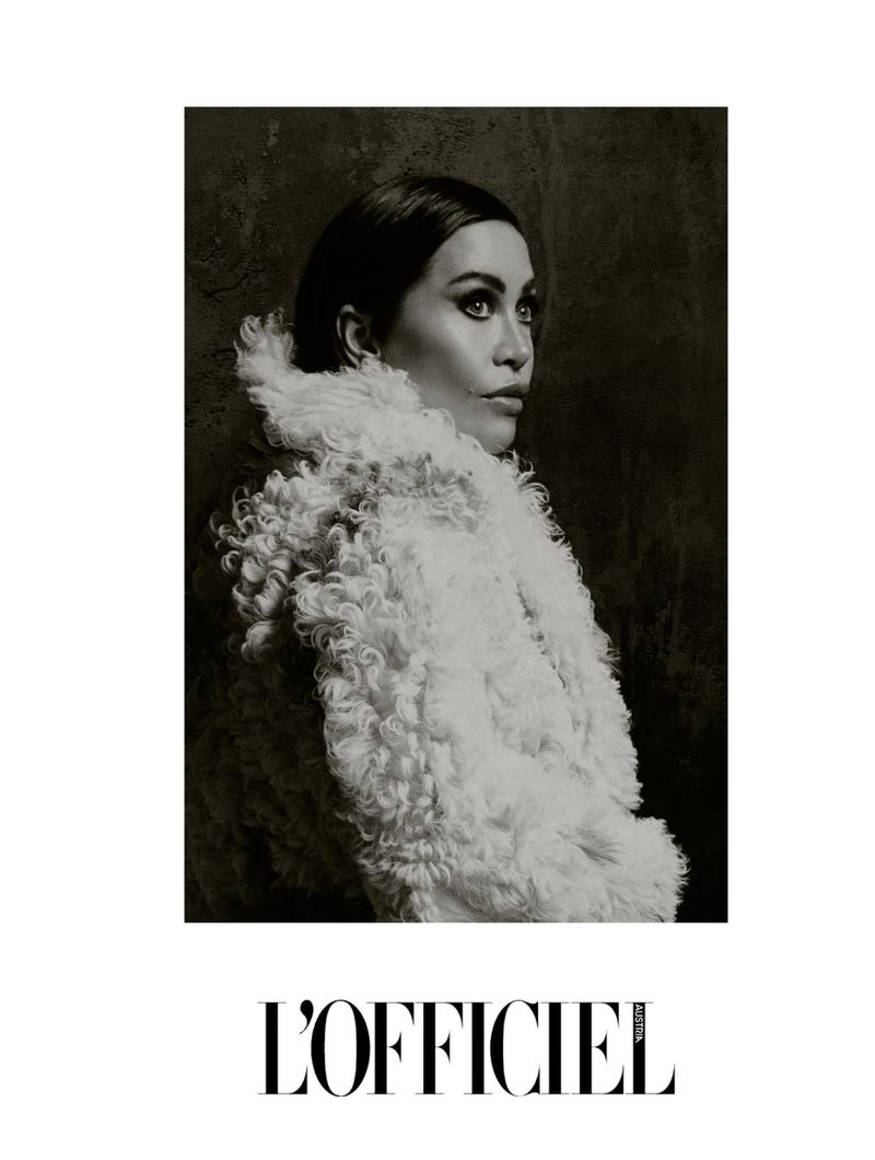 Black and white portrait of an adult female model in a white textured coat, looking right against a dark background.