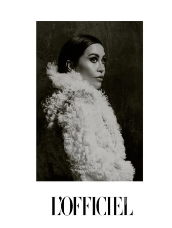 Black and white portrait of an adult female model in a white textured coat, looking right against a dark background.