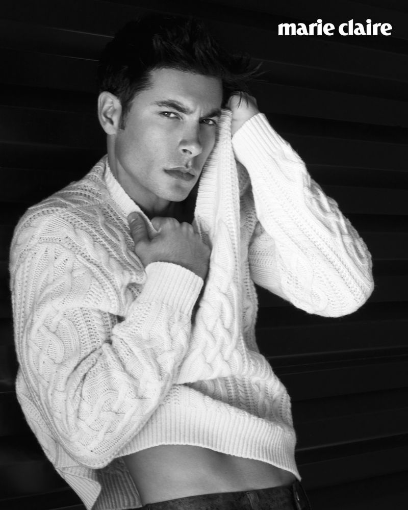 Handsome man poses in a white cable-knit sweater against a dark background, showcasing a blend of style and classic portraiture.