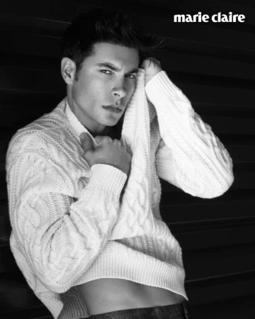 Handsome man poses in a white cable-knit sweater against a dark background, showcasing a blend of style and classic portraiture.