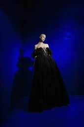 Model wearing a voluminous black gown standing against a deep blue textured background