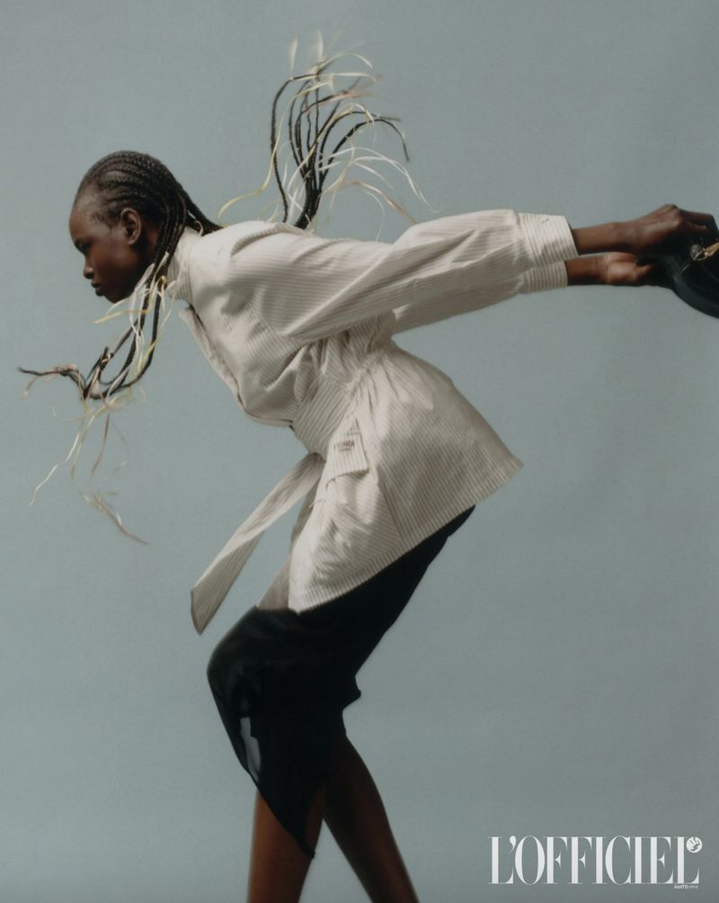 Fashion shot of an African woman in a striped jacket and black skirt with braided hair, dynamically posed against a solid backdrop.