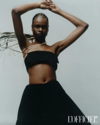 Model Bakhita Lual with braided hair posing in a black strapless top against a pale grey studio seamless backdrop for L'Officiel Italia.