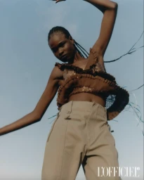 Model Bakhita Lual wearing a brown crop top and tan trousers against a clear sky background for L Officiel Italia.