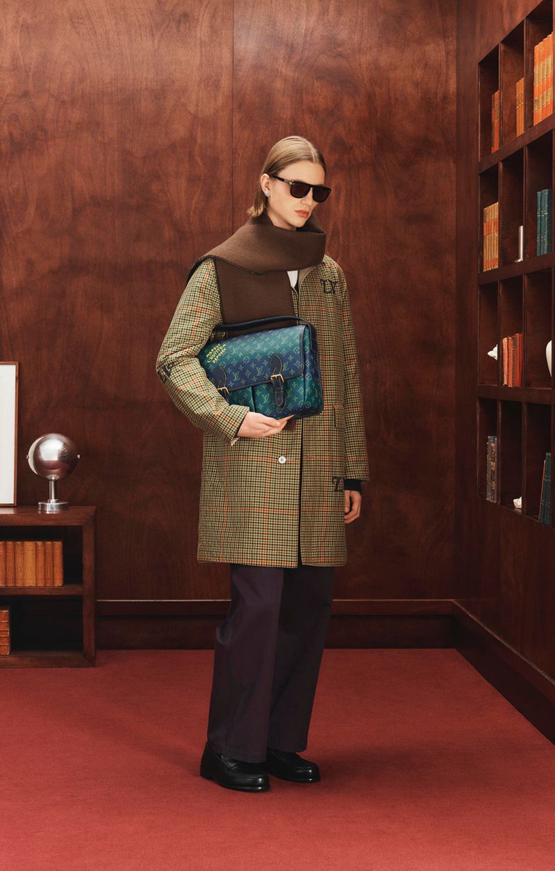 Stylish person in plaid coat and brown scarf holding a blue-green handbag in a room with wooden walls and a bookshelf, fashion shot.