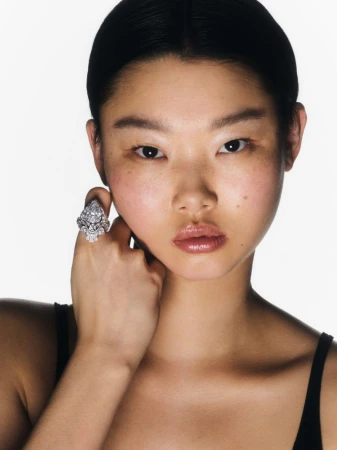 Close-up shot of an Asian female wearing a large diamond ring, eyes forward, set against a bright white background in a beauty editorial.