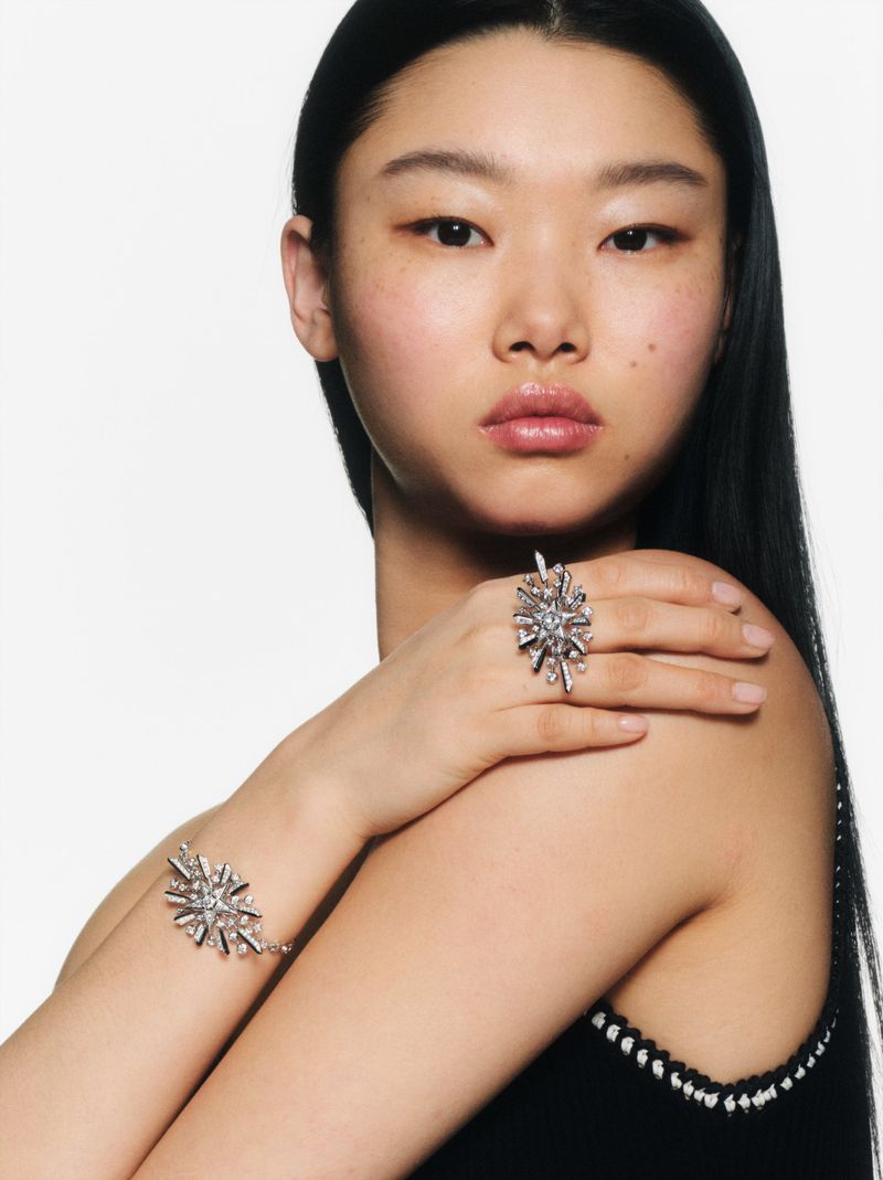 Close-up of an Asian woman showcasing jewelry, including a ring and a bracelet, on a bright, white background in a studio shot.