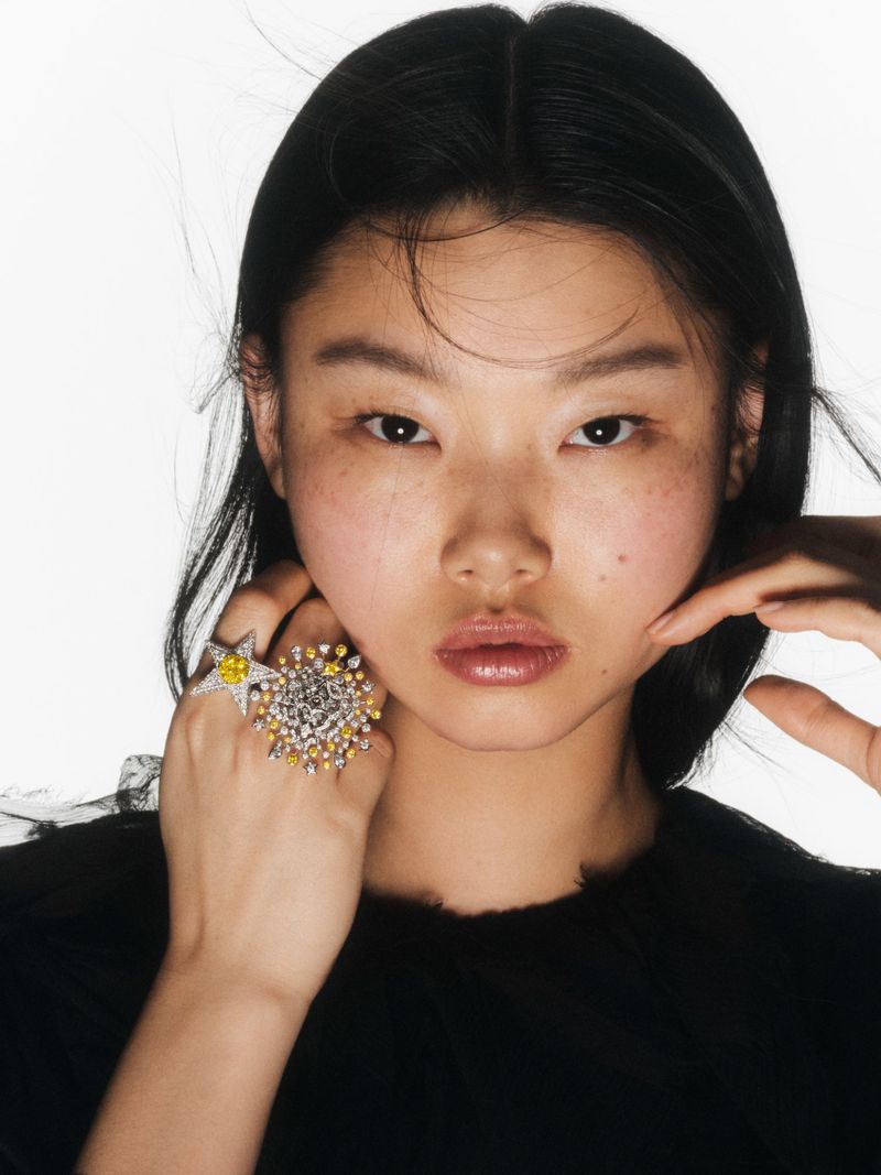 Close-up of a young Asian woman in a black top showcasing starburst statement rings against a stark white background in a beauty shot.