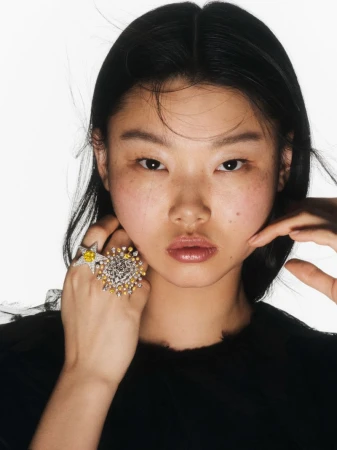 Close-up of a young Asian woman in a black top showcasing starburst statement rings against a stark white background in a beauty shot.