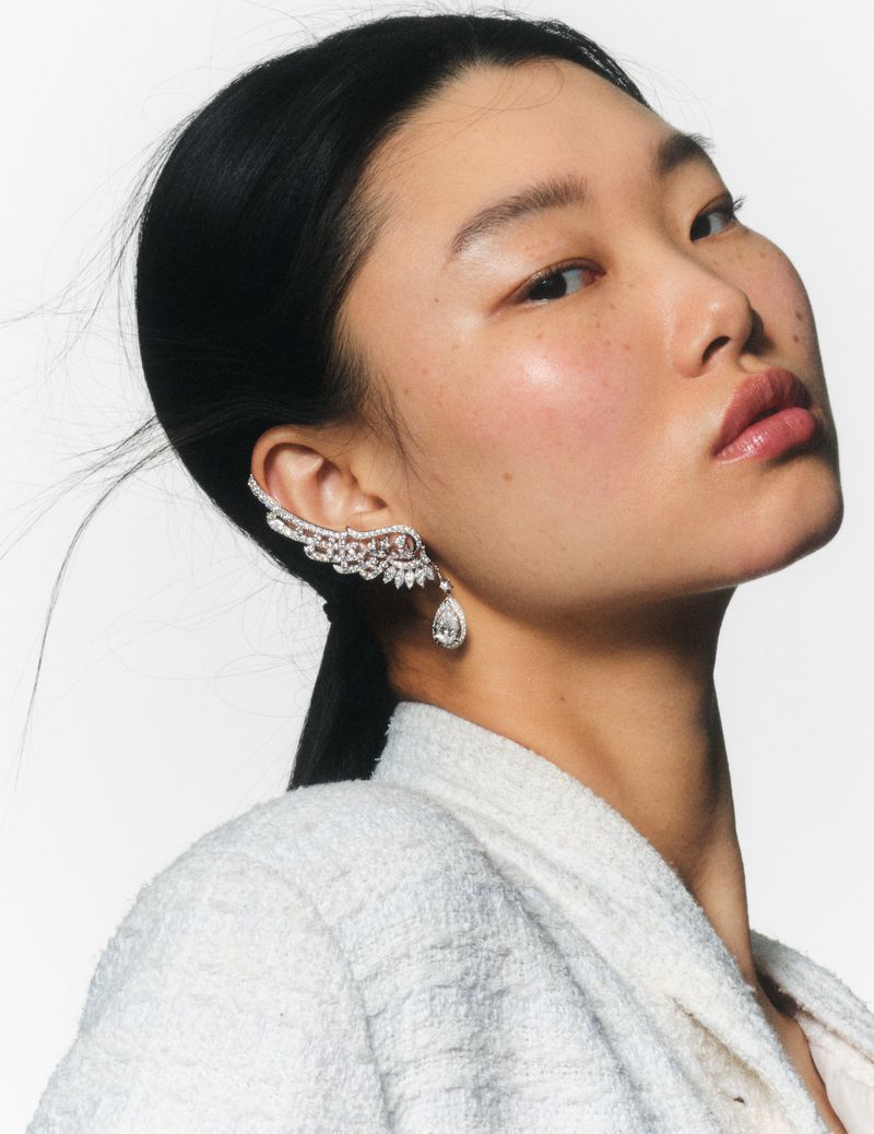 Close-up of an Asian woman wearing a sparkling crystal ear cuff and a white textured jacket, with a clean, light background.