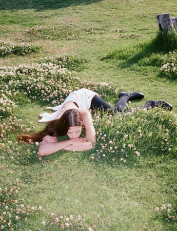 Woman in white dress and black leggings lying in a grassy field with white clover flowers on a sunny day, nature, fashion.