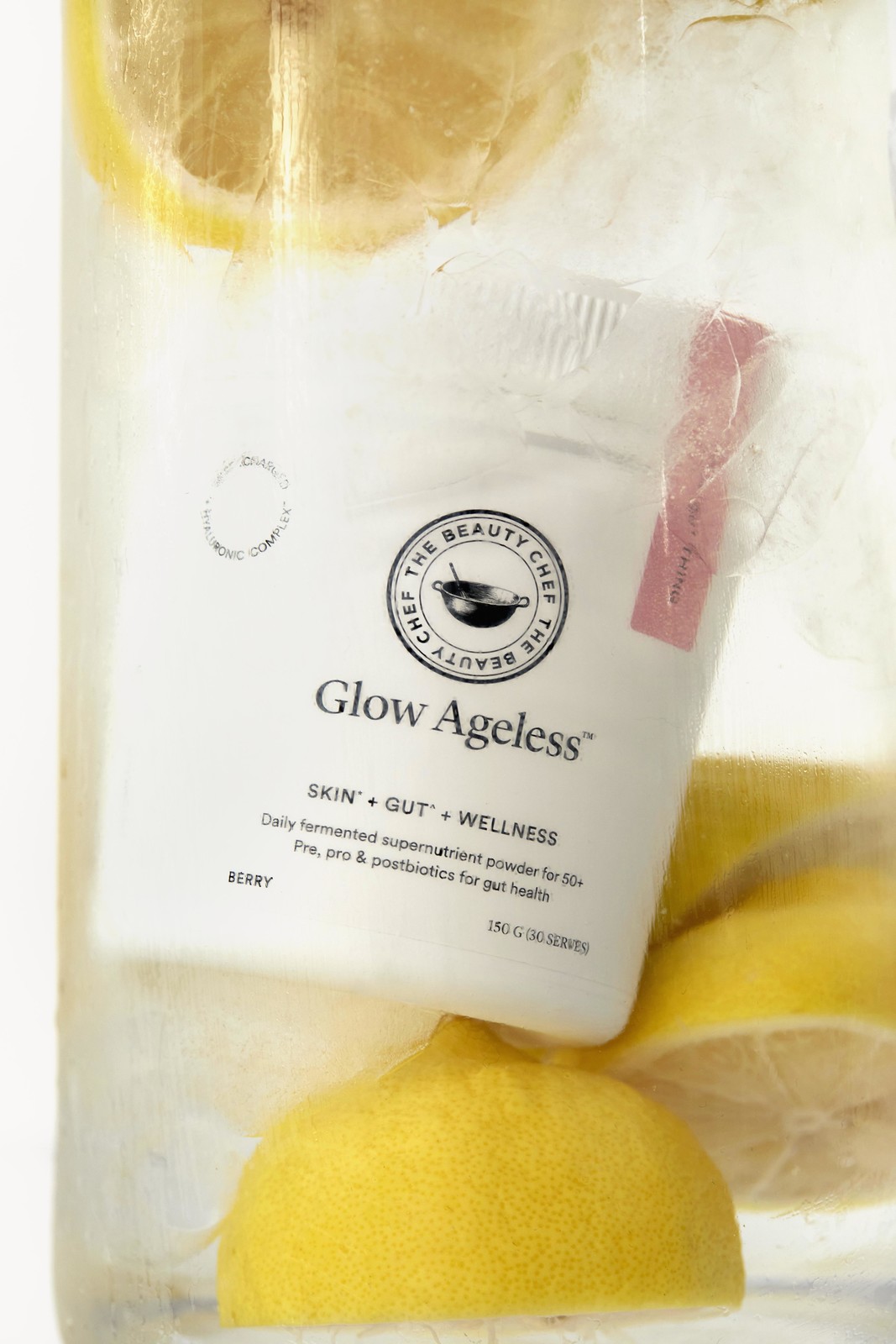 The Beauty Chef Glow Ageless supplement tub is submerged in water with sliced lemons creating a refreshing beauty and wellness image.