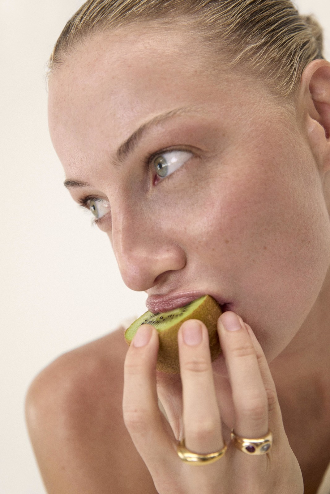 Close-up of a fair-skinned woman eating a slice of kiwi fruit, showcasing vibrant green hues against a neutral backdrop.