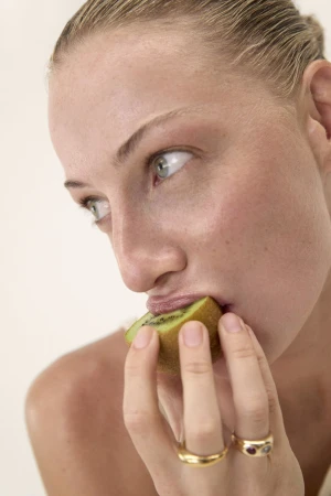 Close-up of a fair-skinned woman eating a slice of kiwi fruit, showcasing vibrant green hues against a neutral backdrop.