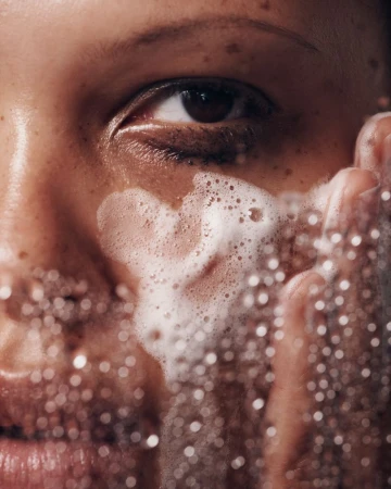 Close-up of an adult female washing her face with a foamy cleanser, highlighting skincare and self-care routine in an indoor setting.