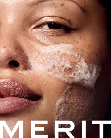 Close-up of a Black adult woman washing her face with foamy cleanser. The beauty shot features freckles, and large text overlay.